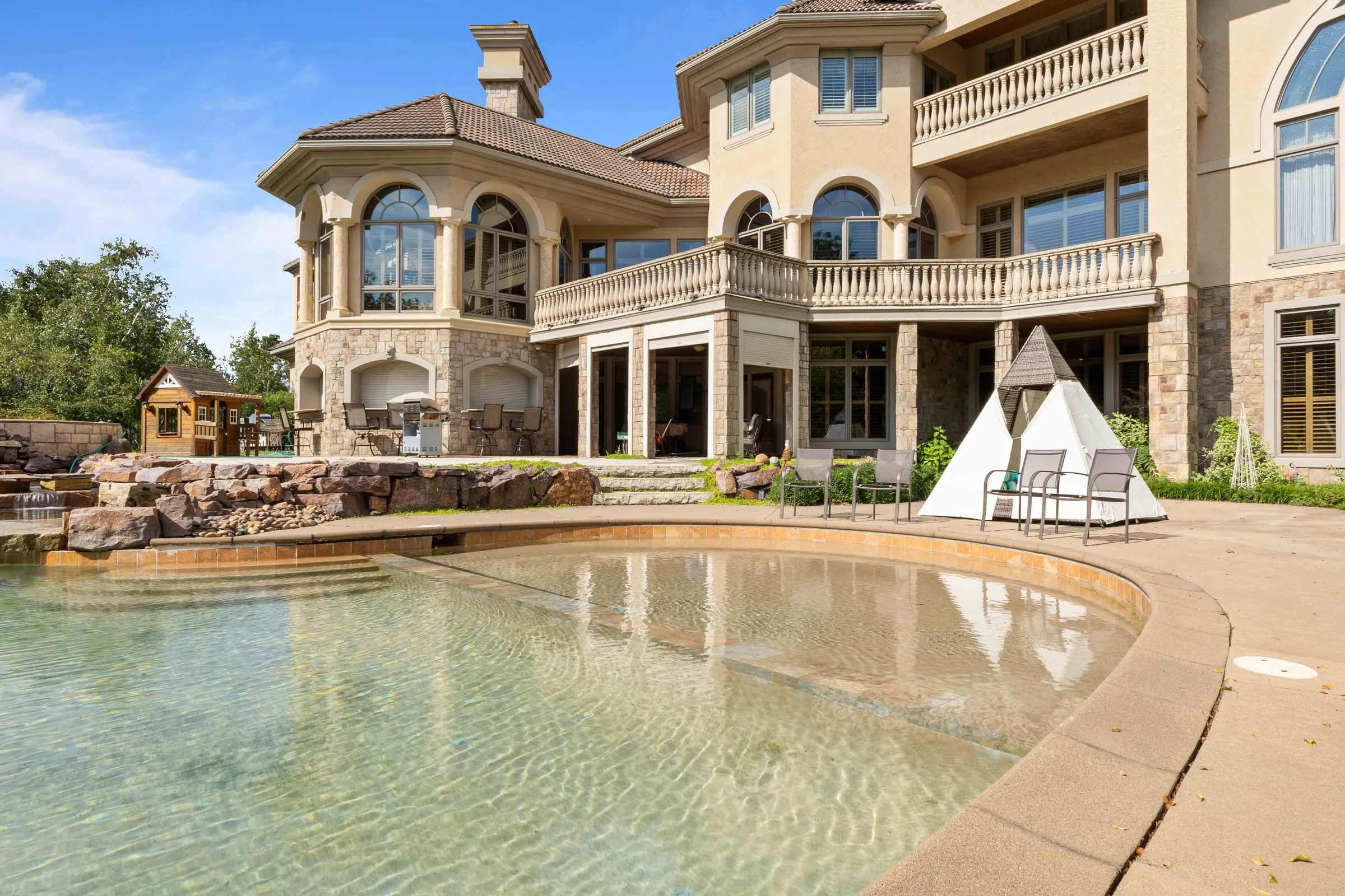 Back of a house with a swimming pool, a covered patio, and a stone water feature.