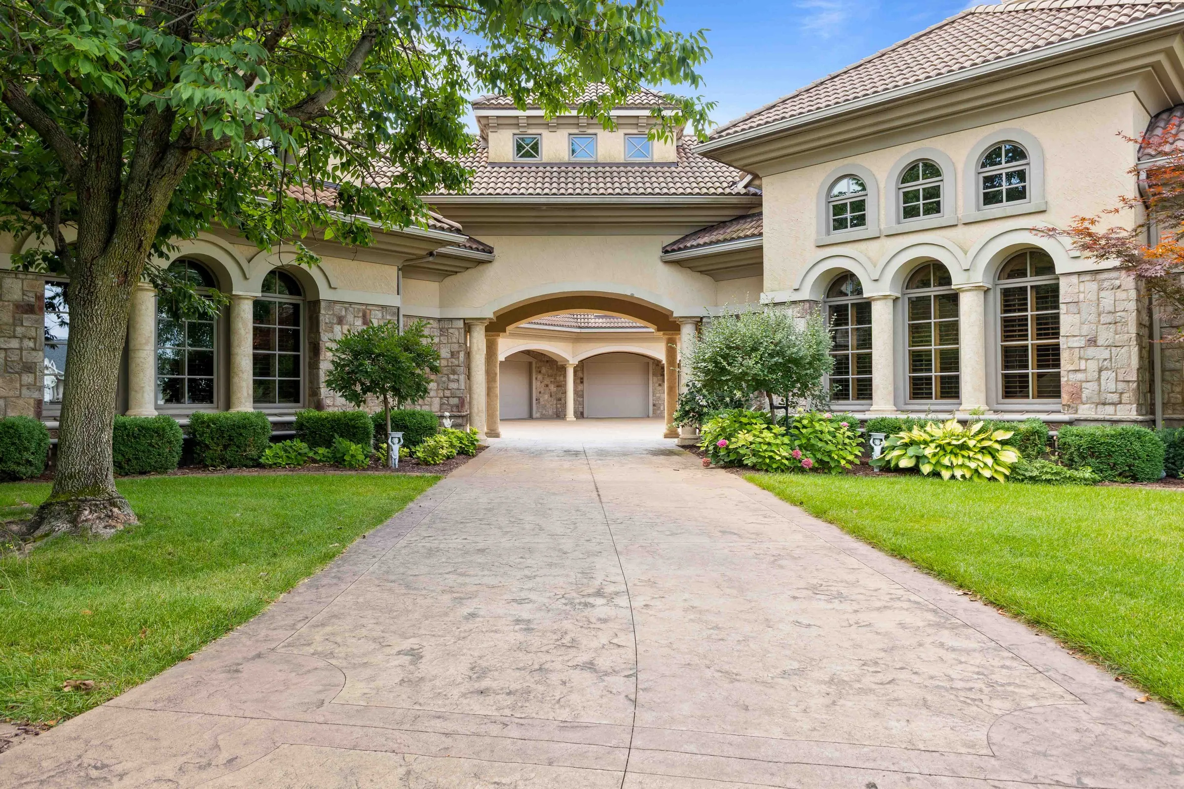 Front of a stone and stucco house with arched windows and a wide driveway.